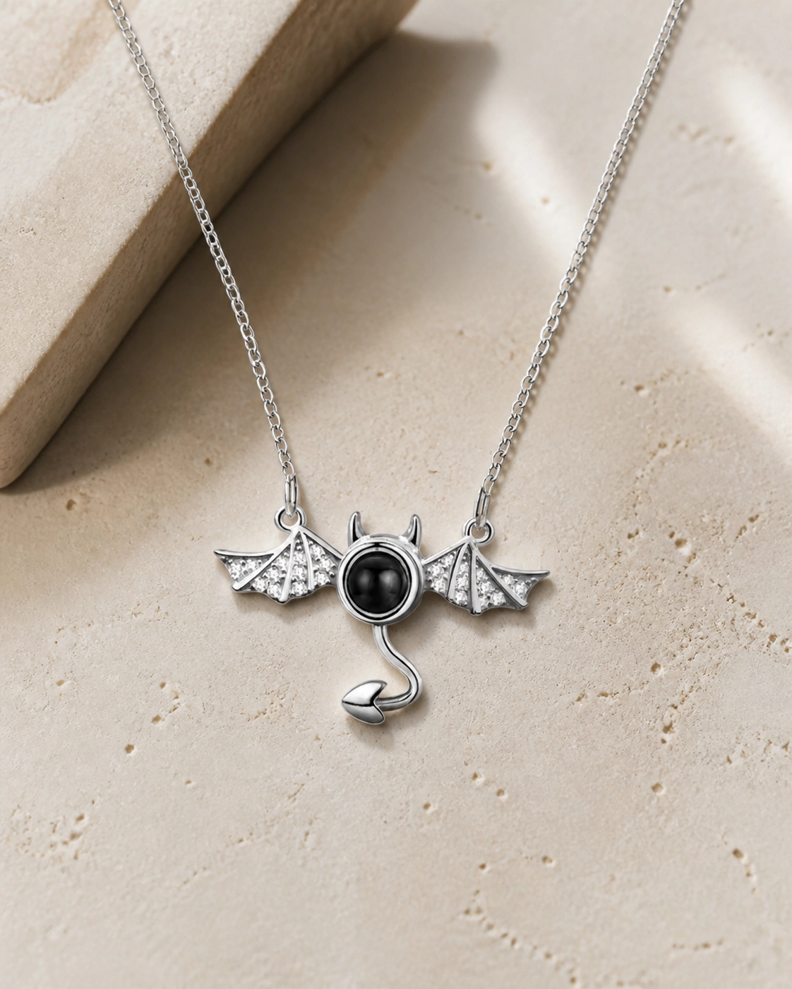 Little Devil photo projection necklace laying on cream stone
